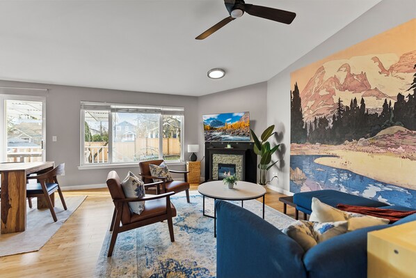 A modern living room with a fireplace, a large painting, and a dining area with wooden furniture. - Modern 3BD house in walkable Ballard, family and dog-friendly, A/C, fenced yard (Seattle)