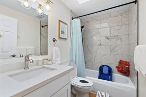A modern bathroom with a white sink, a toilet, a shower with a blue chair, and a marble-tiled wall. - Modern 3BD house in walkable Ballard, family and dog-friendly, A/C, fenced yard (Seattle)