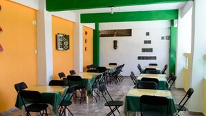 Un espace repas avec des tables et des chaises, une décoration aux couleurs vertes et oranges, et des éléments décoratifs tels que des tranches de pastèque et des fleurs sur les murs.