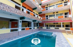 A multi-story hotel with a central courtyard pool, balconies, and a sign indicating the hotel name and location. - Hotel Villas del Plan (Tecolutla)