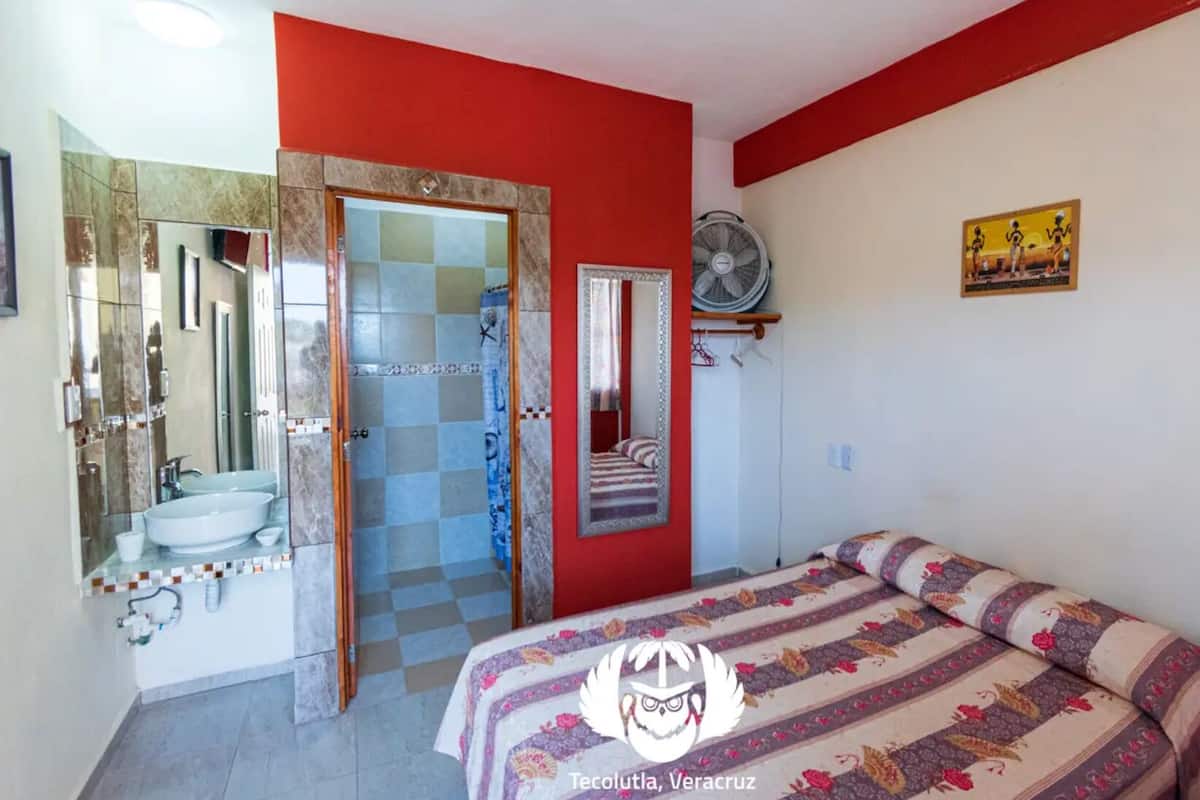 A bedroom with a bed, a bathroom with a shower, and a mirror.