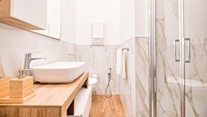 Un bany modern amb un gran mànec blanc, un armari de tocador de fusta, parets de marbre i una cabina de dutxa de vidre.