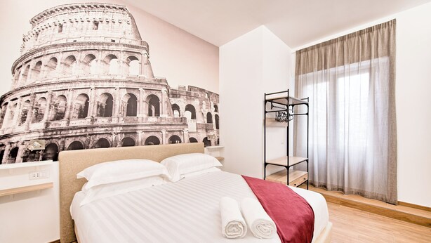 Habitació d'hotel amb un llit, una tauleta de nit, una estantanya penjada a la paret i una finestra amb cortines.