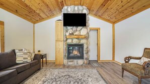 A living room with a stone fireplace, wooden ceiling, and a patterned rug. - Lovely Lakehouse by Grand Traverse Bay. Pet Friendly! (Traverse City)