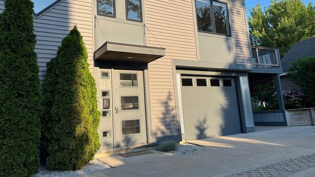 A two-story house with a garage, a covered entryway, and a small porch. - SUNSET PLACE (Grand Haven)