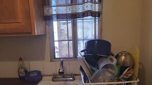 Una cocina con un lavabo, una ventana con cortinas de encaje y un escurreplatos lleno de platos.