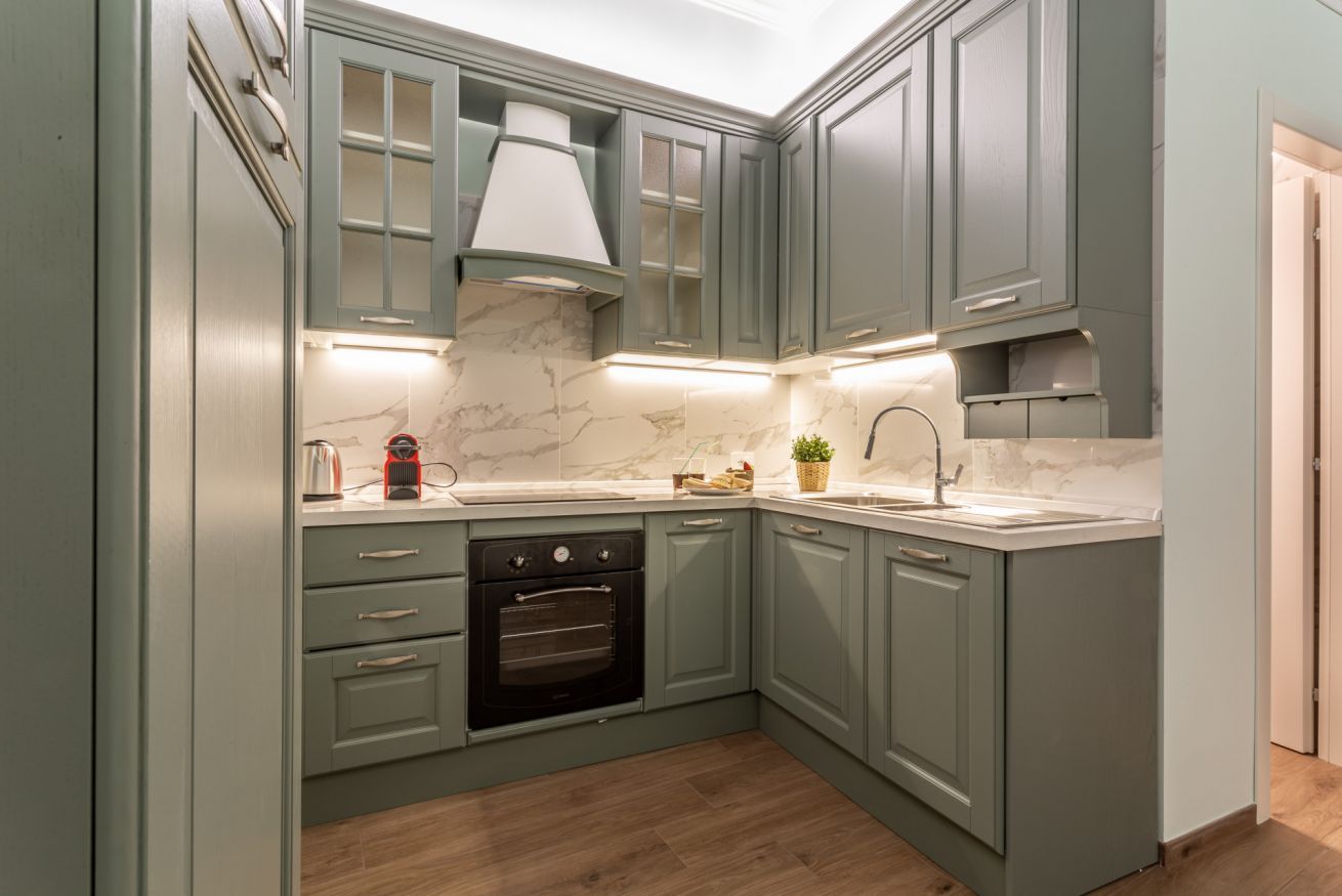 A kitchen with light green cabinets, a marble backsplash, a built-in oven, and a sink.