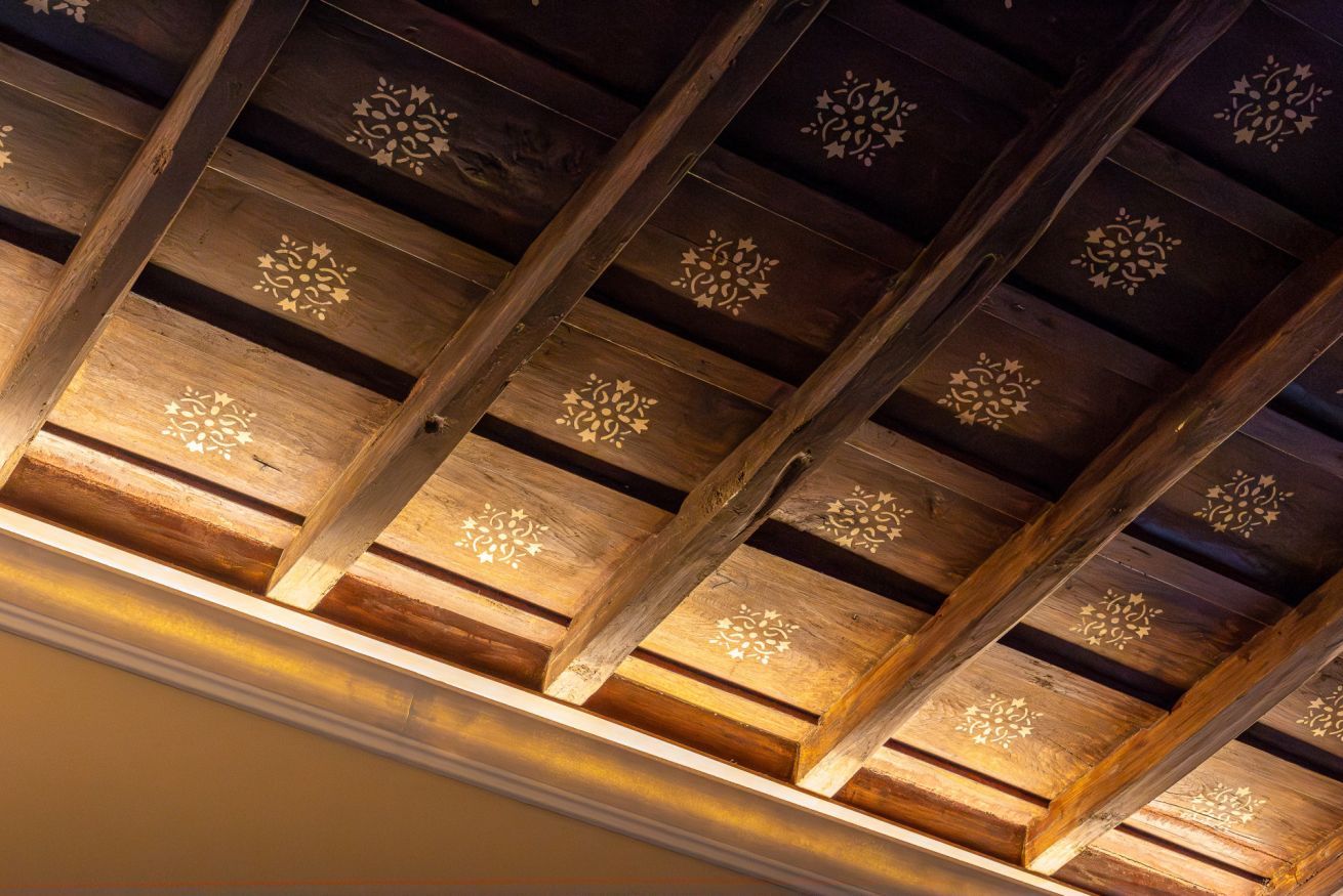 A ceiling with wooden beams and decorative patterns.