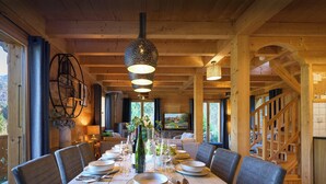 Een eetruimte met een houten tafel voor zes personen, omringd door stoelen, met een groot raam en uitzicht op het landschap.