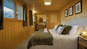 Een houten kamer met een bed, een nachtkastje, een spiegel en ingelijste botanische prints aan de wand.