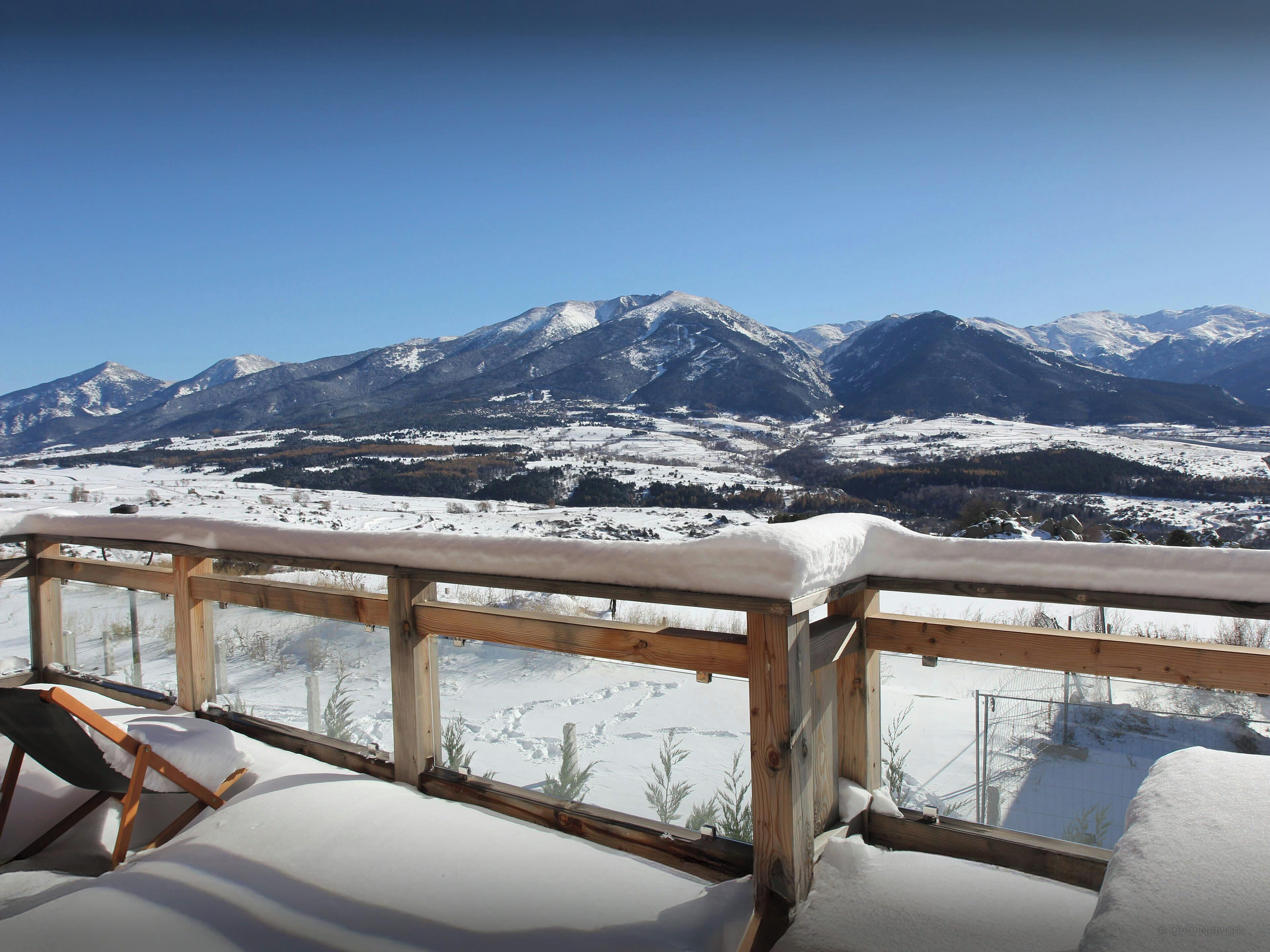 A snow-covered mountain view from a wooden deck with a chair and a table.