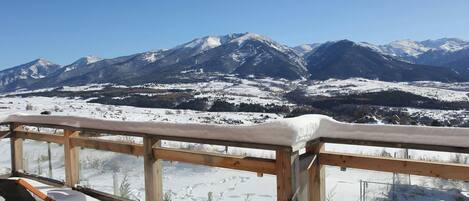 A snow-covered mountain view from a wooden deck with a chair and a table.