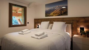 A neatly made bed with white linens and towels, a wooden headboard, and a painting of a mountain landscape on the wall.