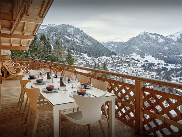 Un coin repas avec une table dressée pour quatre personnes, donnant sur une ville de montagne enneigée.
