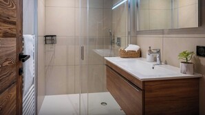 A modern bathroom with a glass shower enclosure, a wooden vanity with a white countertop, and a large mirror above the sink.