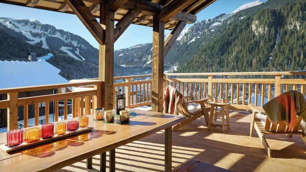 Eine Holzterrasse mit einem Tisch für zwei Personen mit Blick auf eine verschneite Berglandschaft.