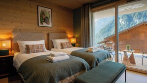 Ein Hotelzimmer mit zwei Betten, einer Bank, einem Tisch mit Stühlen und einem großen Fenster mit Bergblick.