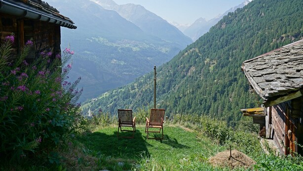 A rustic wooden cabin with two wooden chairs facing a mountainous landscape. - Authentic, beautiful chalet, from 1679. Refurbished. At an altitude of 1,800 m. (Törbel)