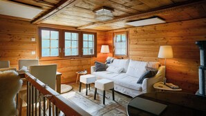 A cozy cabin interior with wooden walls, a white sofa, two white chairs, a small table, and a lamp. - Authentic, beautiful chalet, from 1679. Refurbished. At an altitude of 1,800 m. (Törbel)