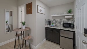 A compact kitchen with a microwave, sink, and stainless steel refrigerator. There is a small bar area with stools and a potted plant.