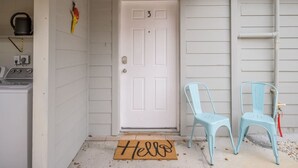 A white door with the number 3, two light blue chairs outside, and a 'Hello' mat on the ground.