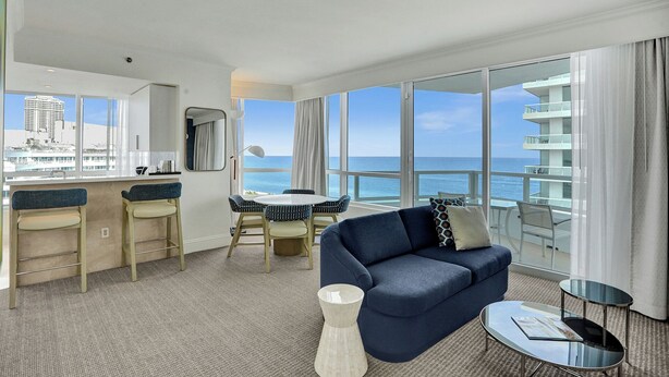 A modern hotel room with a balcony, a dining area, and a sofa.