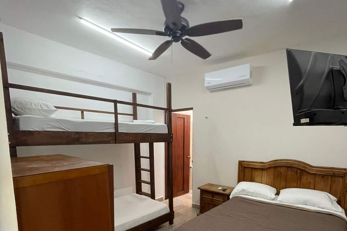 Une chambre avec des lits superposés, un lit simple, un ventilateur de plafond, un climatiseur et un téléviseur.
