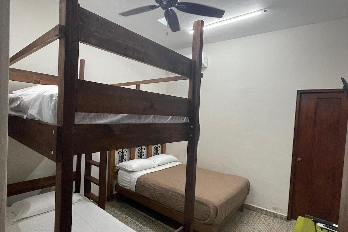 Une chambre avec un lit superposé, un ventilateur de plafond, des carreaux de sol à motifs et un petit bureau avec une chaise.