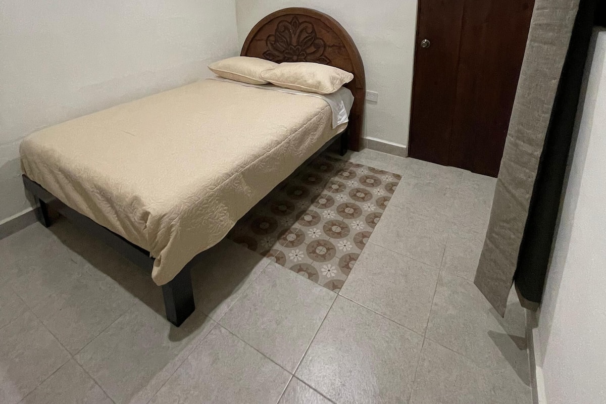 Une petite chambre à coucher, bien rangée, avec un lit, un ventilateur de plafond, un climatiseur et une porte.