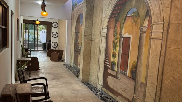 A hallway with a mural of arches and a ceiling fan. There are chairs and tables along the wall.