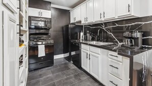 A modern kitchen with white cabinets, a black refrigerator, a stainless steel stove, and a marble countertop.