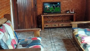 Huoneessa on tiiliseinä, puinen katto, televisio puukorokkeella ja kaksi sohvaa, joissa on värikkäitä koristetyynyjä.