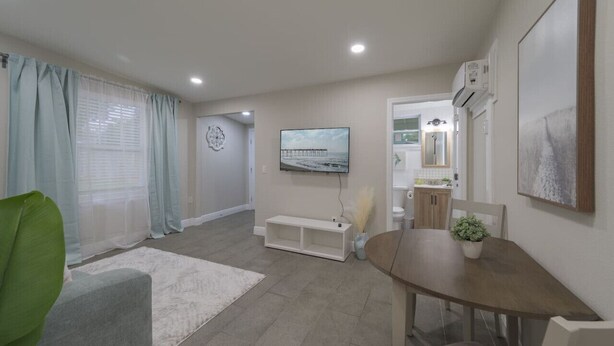 A modern living room with a grey sofa, a wooden dining table, and a TV mounted on the wall. - Comfortable 1 bedroom home (Orlando)