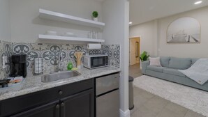 A modern kitchen with a built-in microwave, a coffee maker, and a sink. There is a grey sofa and a plant in the living area. - Comfortable 1 bedroom home (Orlando)