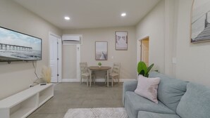 A living room with a grey sofa, a white TV stand, a dining table with chairs, and a white rug. - Comfortable 1 bedroom home (Orlando)