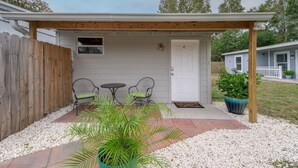 A covered patio with two chairs and a small table, a wooden fence, and a door with the number 4. - Comfortable 1 bedroom home (Orlando)