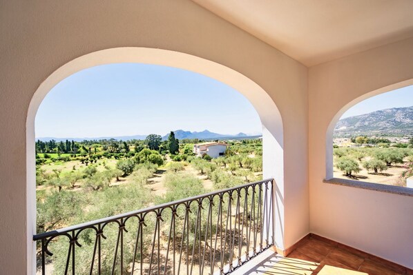 A balcony with a view of a rural landscape, including trees and distant mountains.