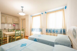 Una habitación con dos camas, una mesa de comedor con sillas, una zona de cocina y un ventanal con cortinas.