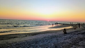 Une plage au coucher du soleil, avec des gens qui se promènent et qui sont assis sur le sable.