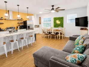 Una cocina moderna con armarios blancos, una zona de comedor con pared verde y un sofá gris con cojines estampados.