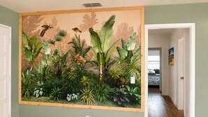 Un couloir orné d’une grande fresque murale représentant des plantes et des oiseaux tropicaux, doté d’un plancher en bois et d’une porte donnant sur une autre pièce.