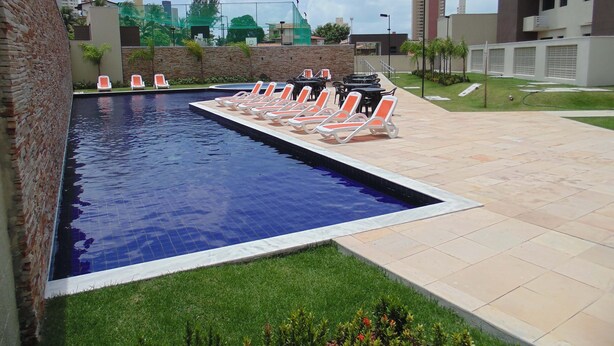 Una piscina con sillas de descanso y una zona ajardinada.