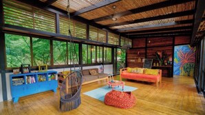 A spacious room with a large window, a blue cabinet, a hanging chair, a red bean bag, and a wooden ceiling. - Deluxe Twin Room (Cahuita)