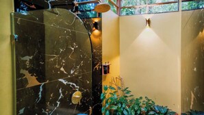 A bathroom with a marble shower enclosure, a blue toilet, and a planter with green plants. - Superior Bungalow (Cahuita)