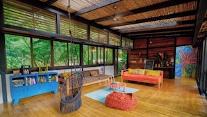 A spacious room with a large window, a blue cabinet, a hanging chair, a red bean bag, and a wooden ceiling. - Superior Bungalow (Cahuita)