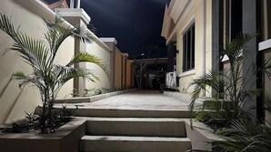 Vista nocturna del exterior de un edificio con escalones que conducen a una entrada cubierta, rodeado de plantas de palma.