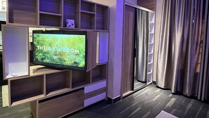 Una sala moderna con una televisión de pantalla plana sobre un mueble de madera, un ventanal corredizo y suelo de madera oscura.