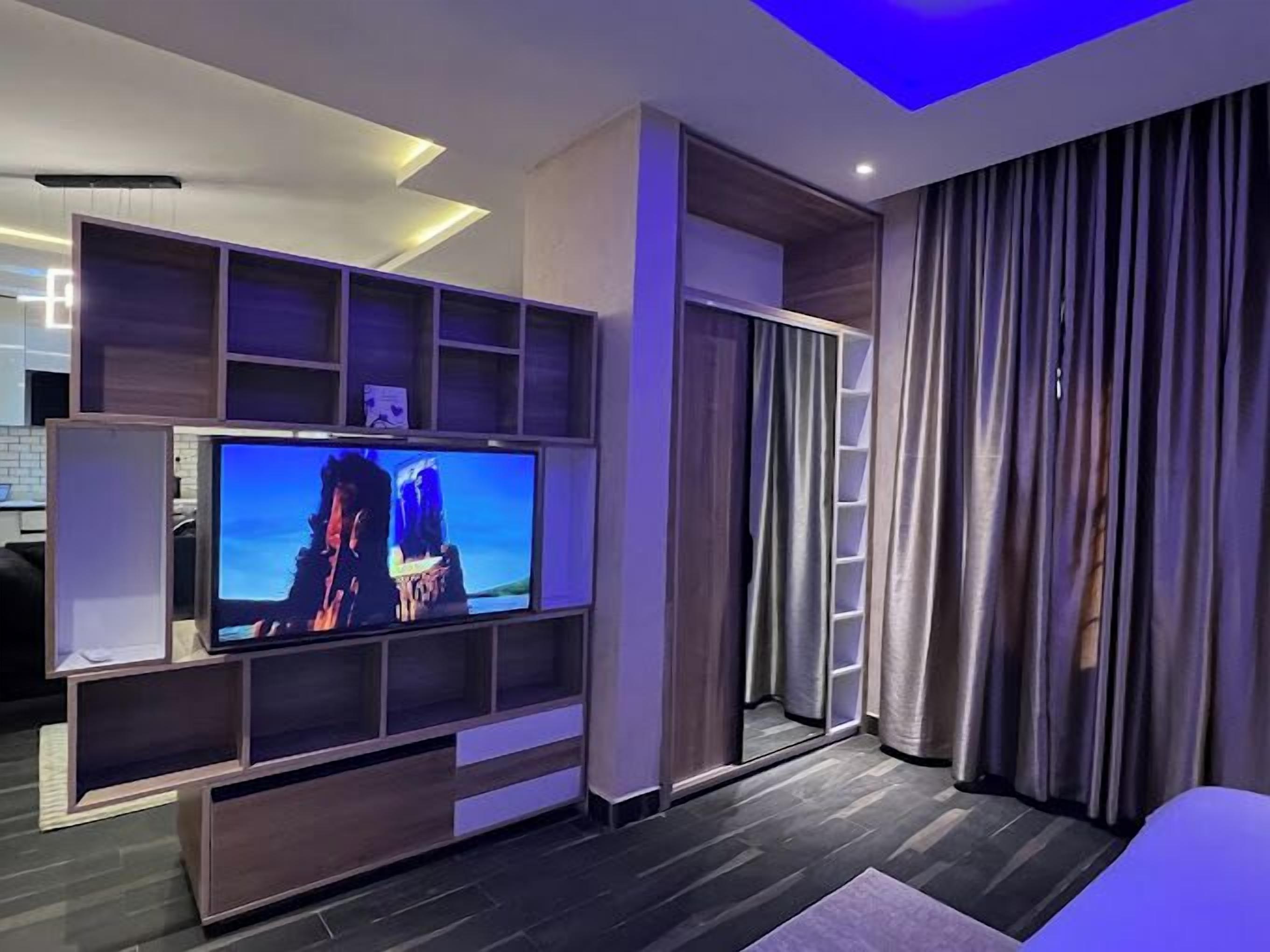 Ein modernes Wohnzimmer mit Flachbildfernseher, integrierten Regalen, einer Schiebetür und einem großen Fenster mit Vorhängen.