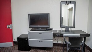 A compact room with a desk, a television, a mirror, and a small refrigerator. - Travelers Rest Motel (San Jose)