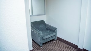 A small, enclosed bathroom with a single grey armchair, a mirror, and a tiled floor. - Travelers Rest Motel (San Jose)